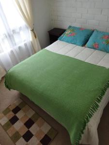 a green blanket on a bed with a window at Casa Valle Volcanes 3 Dormitorios in Puerto Montt