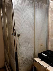Una ducha en una habitación sucia con una puerta de metal. en Cheapest & Strategic Home at Salemba UI, en Yakarta