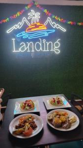 tres platos de comida en una mesa delante de un letrero de neón en The Landing Hotel And Restaurant, en Moyogalpa