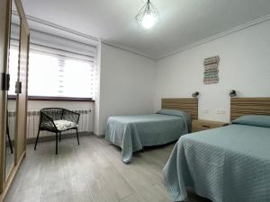 a bedroom with two beds and a chair and a window at CASA SANTI Y LAURA in Cudillero