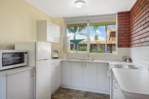a kitchen with white cabinets and a microwave and a window at Kalindo Merimbula in Merimbula