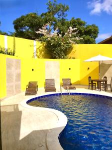 una piscina con sillas y una sombrilla junto a una pared amarilla en Pousada Gente Bonita La Mansion, en Búzios