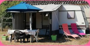 a caravan with a table and chairs and an umbrella at Séjour à la ferme in Vaylats