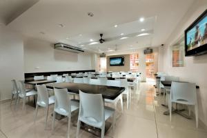 a dining room with white chairs and tables and a flat screen tv at Bahagia Hotel Langkawi in Kuah