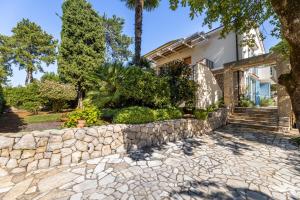 a home with a stone retaining wall and trees at Apartman Fana in Njivice