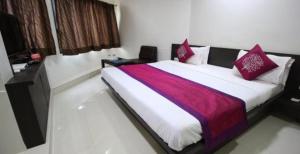a bedroom with a large bed with red and purple pillows at Hotel Nova Cross Road in Rajkot