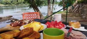 a table with plates of breakfast food and a view of a river at Vikendica DRINSKI DAR in Mali Zvornik