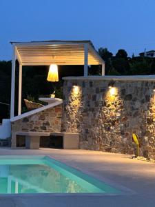a swimming pool next to a stone wall with a pergola at Villa Koukounaria in Skopelos Town