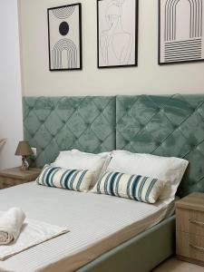 a bed with a green headboard and some framed pictures at Lungomare Luxury Sea View Apartaments in Vlorë