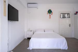 a white bedroom with a bed and a flat screen tv at Kyon Beach Suites Kythnos in Kanala