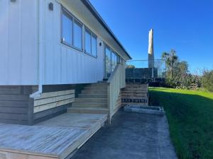 a house with a wooden staircase next to a lawn at Ocean Beach Paradise in Tairua
