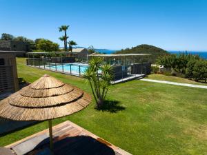 a straw umbrella sitting on a lawn next to a pool at Hôtel U San Daniellu villas et chambres in Saint-Florent