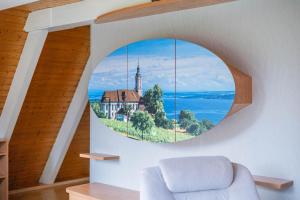 ein rundes Fenster in einem Raum mit einem Haus und einer Kirche in der Unterkunft Ferienwohnpark Immenstaad am Bodensee Nurdachhaus Typ 8 NDT 014 in Immenstaad am Bodensee