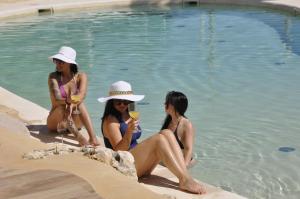 three women sitting in the water next to a swimming pool at Baglio Dello Zingaro in Scopello