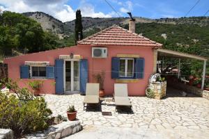 a pink house with blue shutters and two chairs at Mountain Breeze Cottage in Makriótika