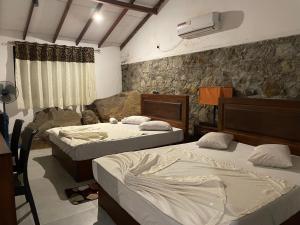 a bedroom with two beds and a stone wall at Citrine Belihuloya in Belihul Oya