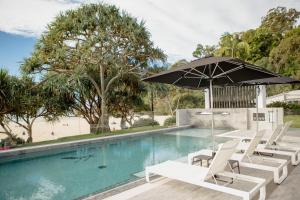 a swimming pool with chairs and an umbrella at Netanya Noosa Beachfront Resort in Noosa Heads