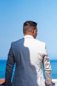 a man in a suit standing in front of the ocean at Evangelia in Karfas