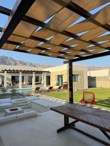 a patio with a wooden pergola and a table at Acacia Sifah in Muscat