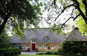 a yellow house with a thatched roof with a red door at Bakkehuset Countryhouse in Skovby