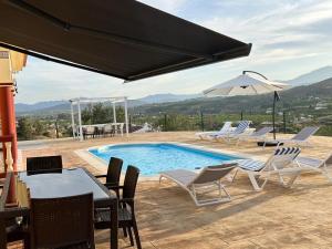 a swimming pool with chairs and a table and an umbrella at Casa Rural Alora Caminito del Rey in Alora