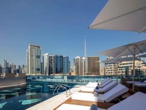 une piscine avec des chaises longues blanches et une vue sur la ville dans l'établissement Hyde Hotel Dubai, à Dubaï