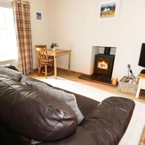 a leather couch in a living room with a fireplace at Cnocachanach Cottage in Tarbert +2 photos