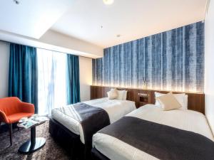 a hotel room with two beds and a chair at Hotel Gracery Sapporo in Sapporo