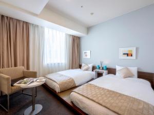 a hotel room with two beds and a chair at Hotel Gracery Sapporo in Sapporo