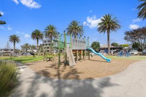 a playground with a slide in a park with palm trees at The Whitianga Sandcastle in Whitianga