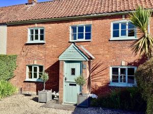 a brick house with a green door and two windows at Tythe Barn Cottage in Glastonbury