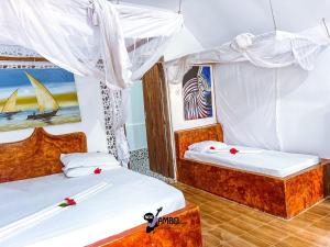 two beds in a room with white curtains at New Jambo Bungalows in Paje