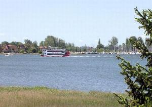 a boat on a large river with trees and buildings at Ferienwohnungen Rosenträger in Kappeln
