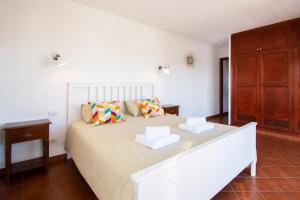 a white bedroom with a large bed and a wooden cabinet at Surfescape Fuerteventura in Lajares