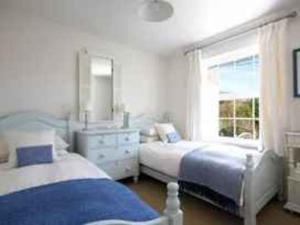 a white bedroom with two beds and a window at Castaway, Port Isaac Bay Holidays in Port Isaac