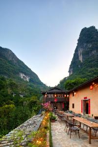 a restaurant with tables and benches and mountains in the background at Yangshuo Yunshe Mountain Guesthouse in Yangshuo