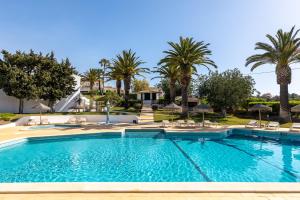 a swimming pool with chairs and palm trees at Parque Monte Verde in Albufeira