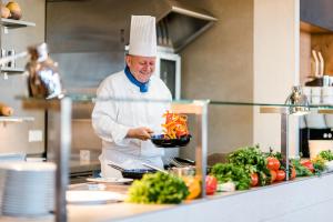a chef in a kitchen holding a plate of vegetables at Strand-Hotel Hübner in Warnemünde