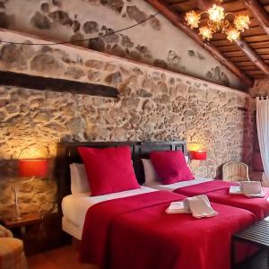 a bedroom with two beds with red sheets and a stone wall at El Zaguán de Cabanillas in Cabanillas del Monte