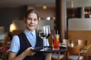 a woman holding a tray with two glasses of wine at Strand-Hotel Hübner in Warnemünde