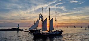 a boat with sails in the water with a lighthouse at Strand-Hotel Hübner in Warnemünde