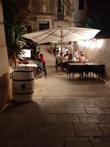 eine Gruppe von Menschen sitzt an Tischen unter einem Sonnenschirm in der Unterkunft Casa del Duomo in Syrakus