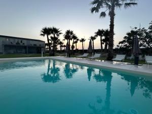 a large swimming pool with chairs and umbrellas and palm trees at B&B Brezza Delle Egadi in Marsala +24 photos