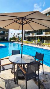 a table with an umbrella next to a swimming pool at Mana Beach 313C - Praia de Muro Alto em Porto de Galinhas in Ipojuca