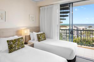 two beds in a hotel room with a balcony at Oaks Sunshine Coast Seaforth Resort in Alexandra Headland