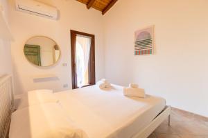 a white bedroom with a bed and a mirror at Villetta con Giardino - Lu Fraili in Nuragheddu