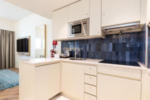 a kitchen with white cabinets and a microwave at Crowne Plaza - Caparica Lisbon in Costa da Caparica
