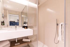 a white bathroom with a sink and a shower at Crowne Plaza - Caparica Lisbon in Costa da Caparica