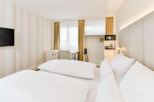 two beds in a hotel room with white pillows at NH Erlangen in Erlangen