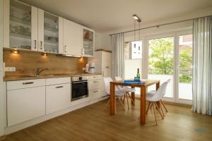 eine Küche mit weißen Schränken und einem Tisch mit Stühlen in der Unterkunft Residenz Hohe Lith Wohnung 04 01 in Cuxhaven